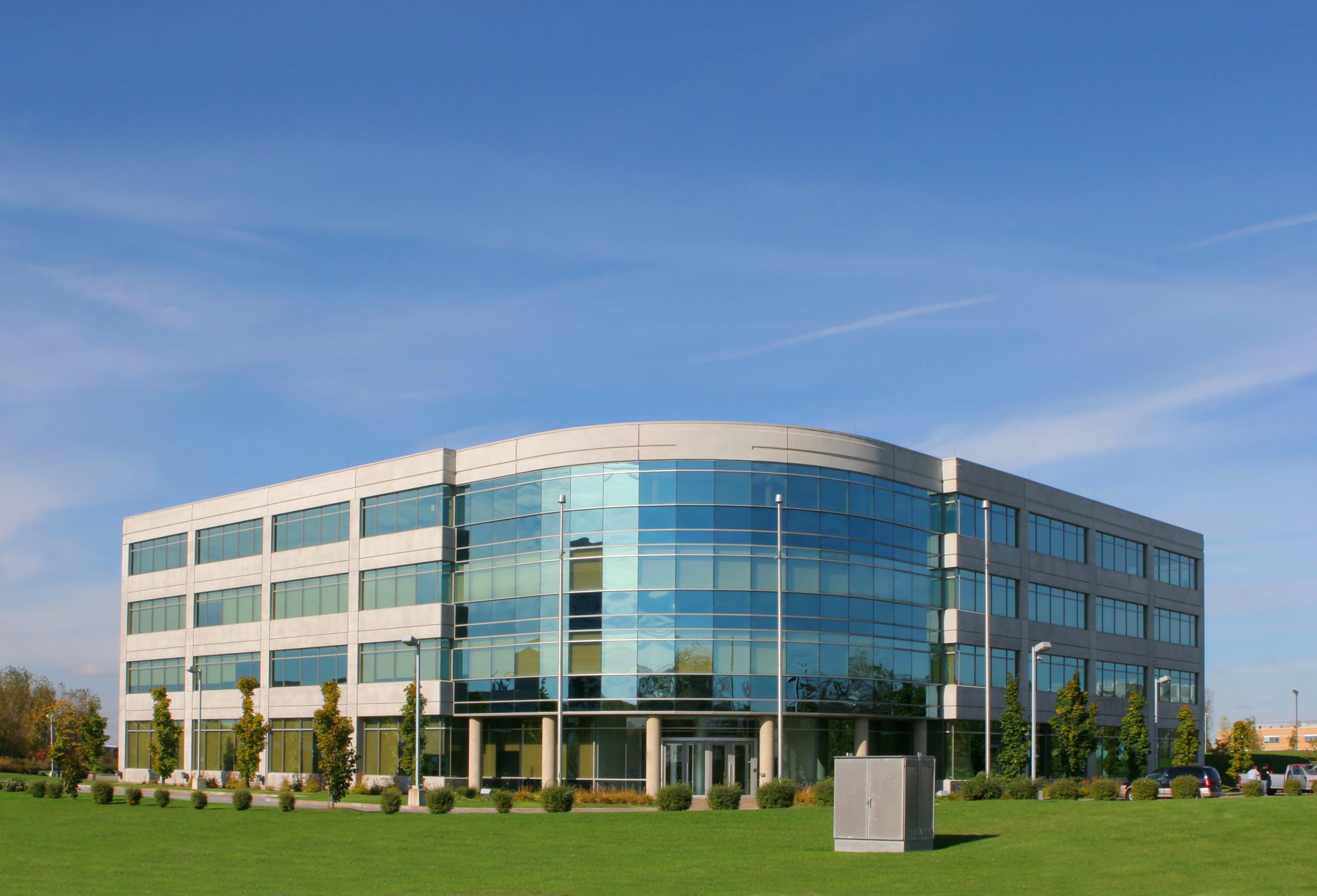 The image depicts a modern office building situated in a suburban market, surrounded by well-manicured landscaping. The building features a sleek exterior facade with large windows that reflect the surrounding greenery. A spacious parking lot is visible in front of the building, providing ample parking space for tenants and visitors. The location in the suburban market makes it an attractive investment opportunity for investors seeking stable returns and long-term growth potential in the commercial real estate sector. The building's strategic positioning and contemporary design make it an ideal choice for businesses looking for a professional and accessible workspace