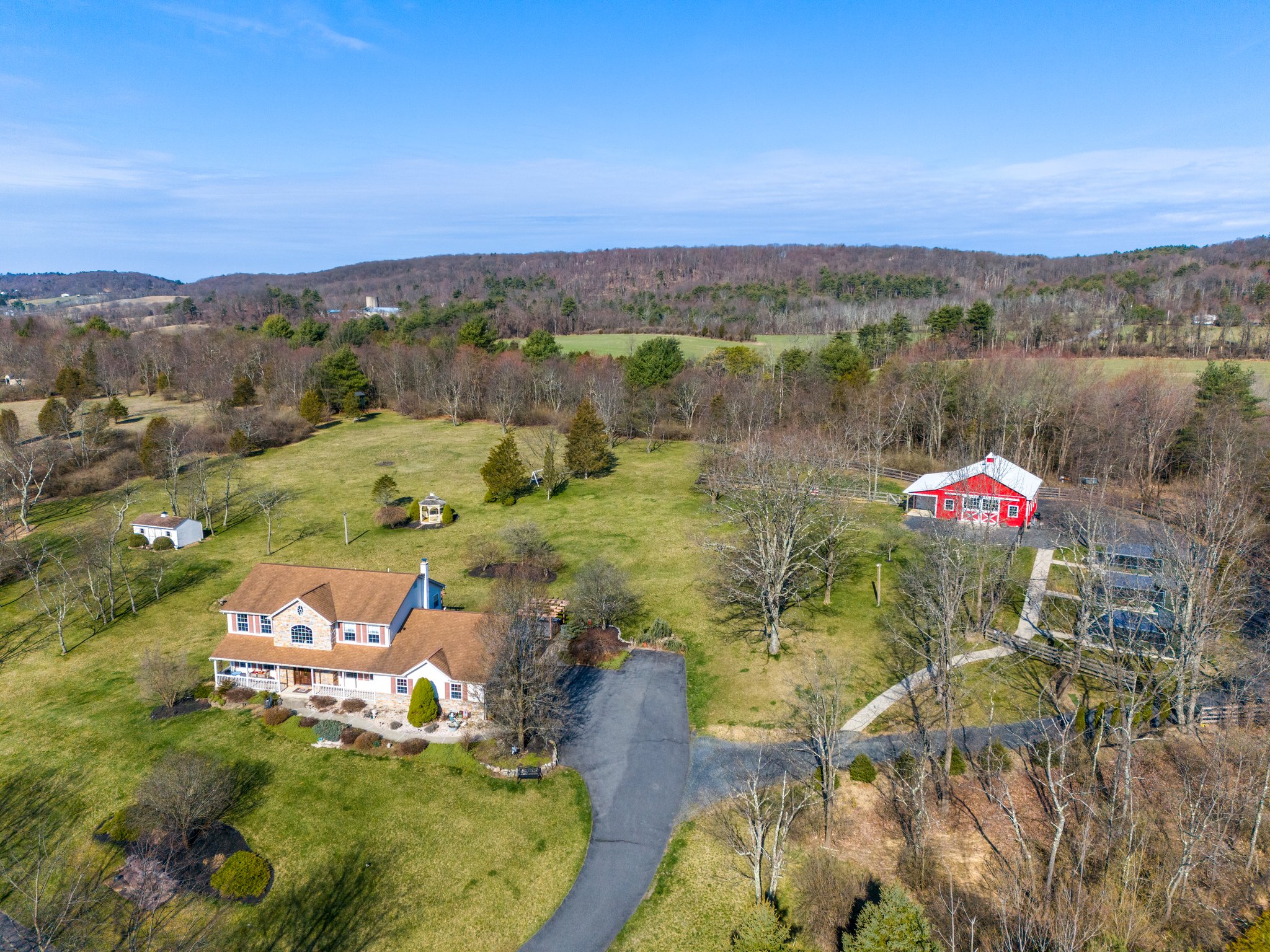 Aerial Photo of a farm for sale in the poconos, featuring a large colonial home with covered front porch and a horse barn and pasture in the back.